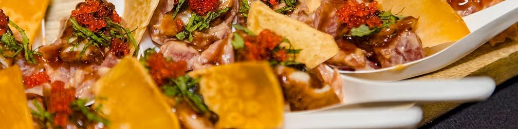 Assorted canap&eacute;s with cured meat, topped with red caviar, herbs, and cheese crisps on a platter.