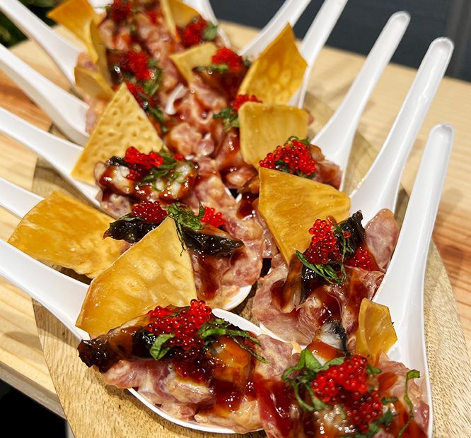 A platter of bite-sized cured meat topped with red caviar-like beads and herbs, served with crisp cracker-like chips.