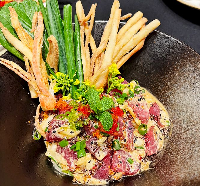 Open-faced tart on a plate topped with prosciutto, green herbs, and crispy fries.