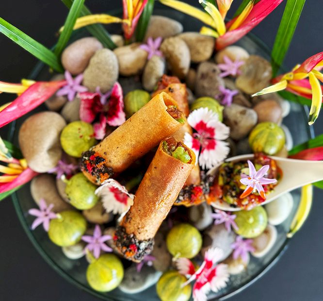 A colorful fruit-and-flower dish with two fried spring rolls nestled among grapes, nuts, and pink-white blossoms.