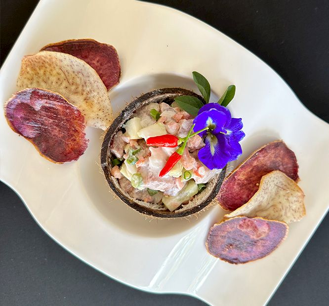 Seafood ceviche/tuna tartare with a purple edible flower, served in a coconut bowl with fried potato chips.