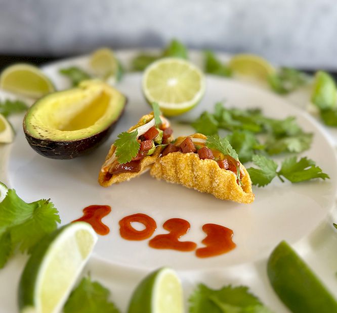 A white platter with a crispy taco/fish dish, salsa, guacamole, cilantro, and lime wedges, with &ldquo;100%&rdquo; written in sauce.