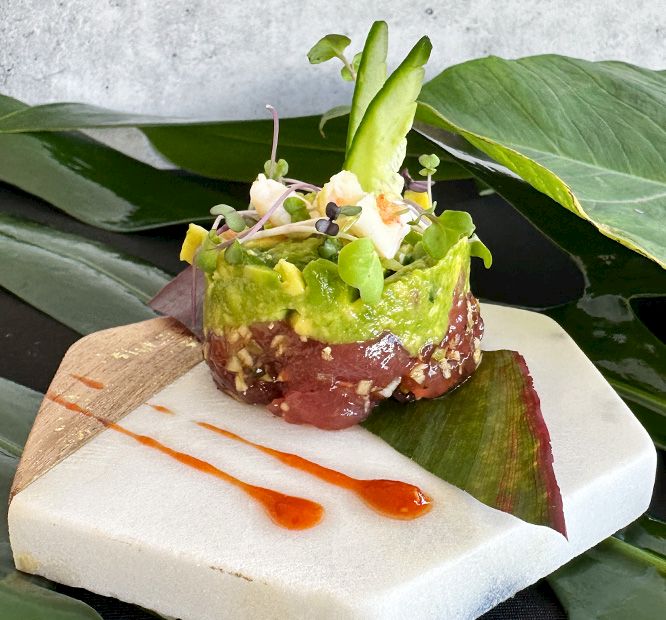 A plated steak topped with guacamole, microgreens, and citrus oil on a banana leaf, garnished with sprouts.