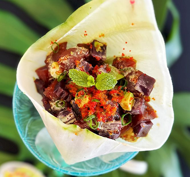 A leaf-shaped taco filled with chopped meat, herbs, mint, and red chili powder, topped with lime and green garnish.