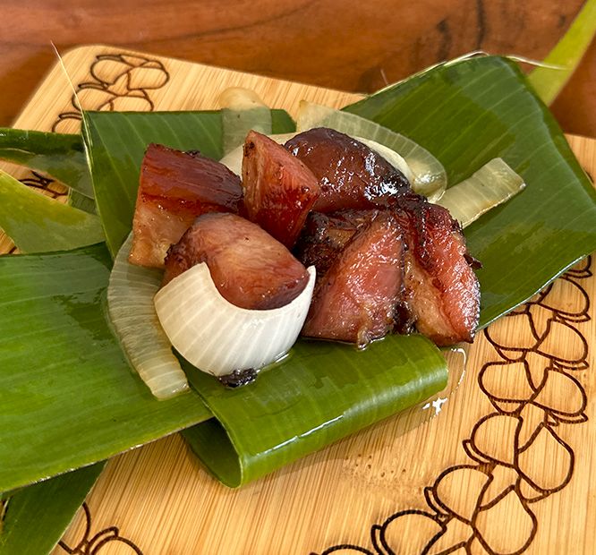 A plate of braised pork and garlic served on banana leaves, shown on a wooden tray.