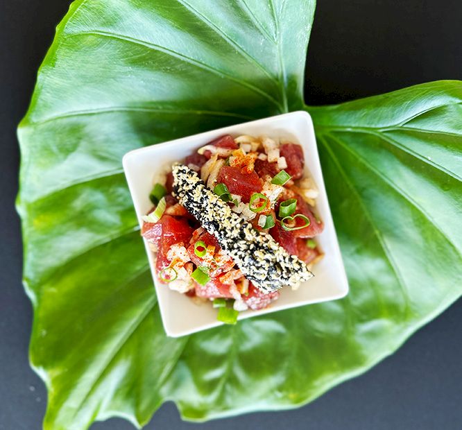 A small square bowl of chopped watermelon-and-tuna salad topped with sesame seeds, resting on large green leaves.